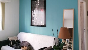 A living room with a teal wall, a white sofa, a framed picture, a lamp, and a mirror. - 2-room apartment for 2 people close to Moure Rouge beach. (Cannes)