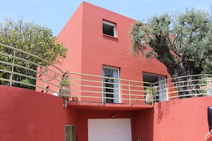 Un bâtiment rouge avec une porte de garage blanche, un balcon doté d’une balustrade et un arbre en arrière-plan.