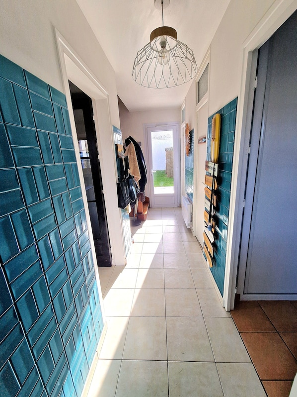 A hallway with a tiled floor, a hanging light fixture, and a door leading to a garden.