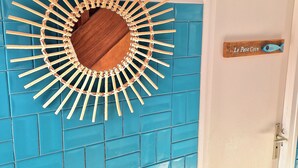 Een blauwe tegelwand met een houten zondecoratie en een deur met het bordje 'Le Petit Coin'.