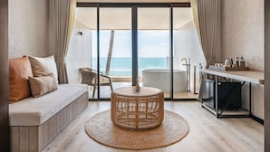 Una habitación moderna con sofá, una mesita de mimbre, vista al océano, bañera y una zona de cocina.