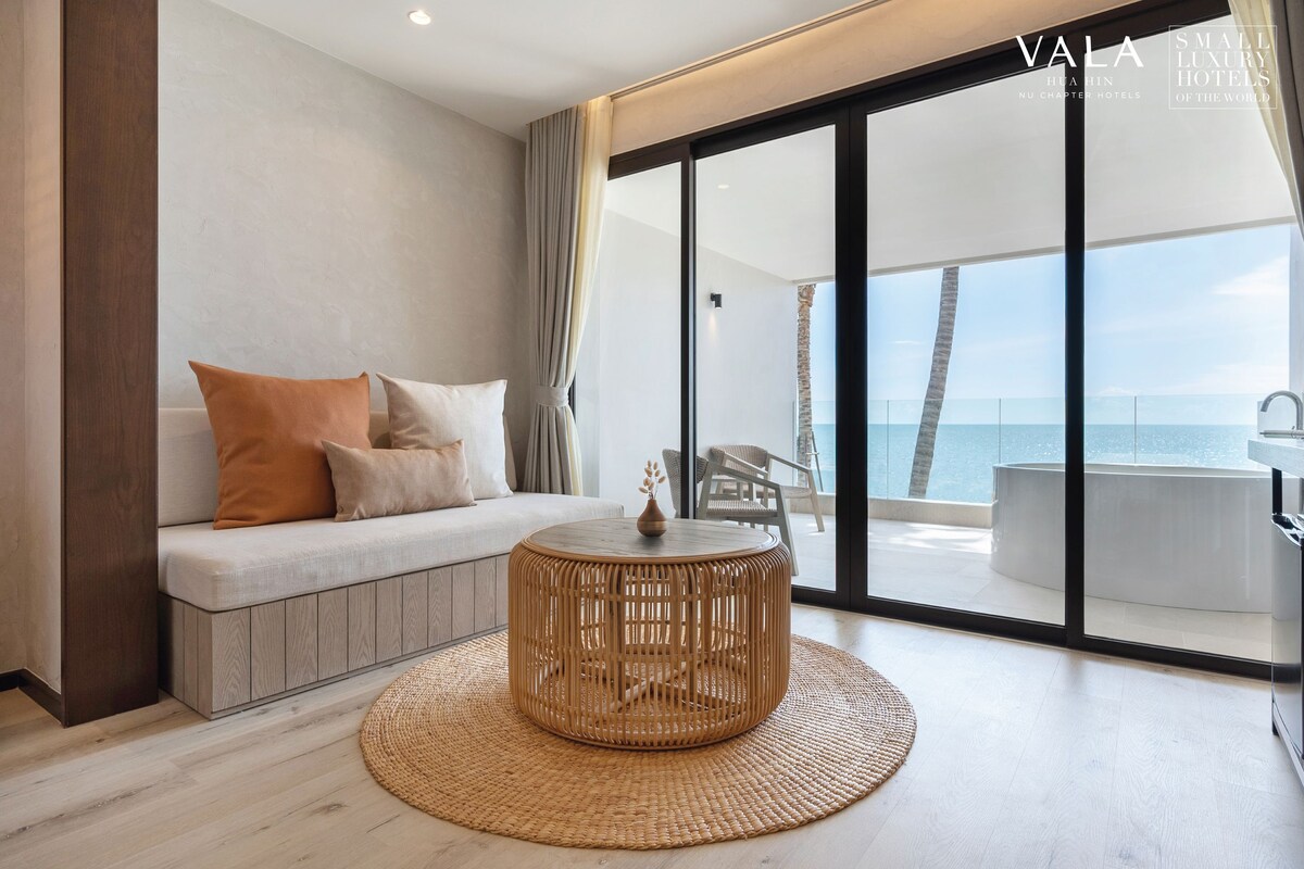 A modern living room with a sofa, a round wicker coffee table, and a view of the ocean through large sliding doors.
