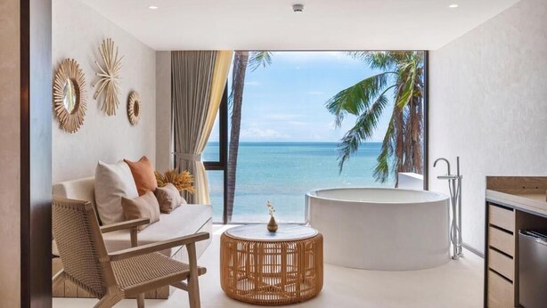 Una habitación moderna con un ventanal grande, una mesa de centro redonda de madera, un sofá blanco y una bañera independiente.