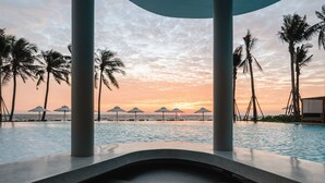 Vista de la piscina con palmeras y sombrillas, con vista al océano al atardecer.