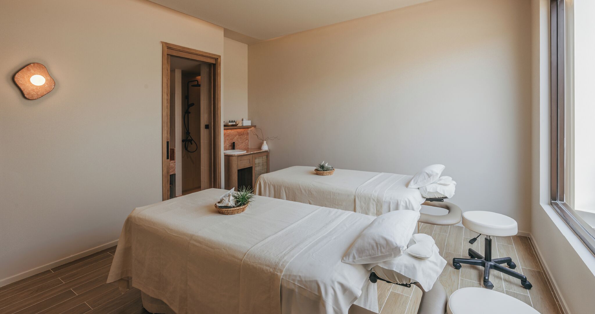 Un cuarto de spa con dos camillas, un lavamanos pequeño y una ventana.