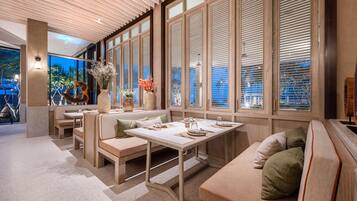A modern interior with a dining area, seating arrangements, and large windows with blinds.