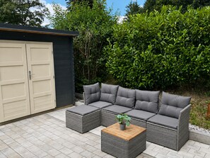 A sectional sofa with cushions, a small wooden coffee table, and a grey wicker chair. - Vacation Home in Bavaria, 88 m², 3 bedrooms, balcony, Wi-Fi (Siegsdorf)