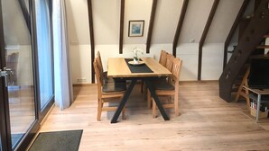 A dining area with a wooden table and chairs, a small vase with flowers, and a staircase to the right. - Vacation home Bavaria, 88 m², 3 bedrooms, balcony, WLAN (Siegsdorf)