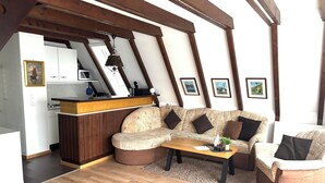 A cozy living area with a wooden ceiling, a sofa set, a coffee table, and a kitchen in the background. - Vacation home Bavaria, 88 m², 3 bedrooms, balcony, WLAN (Siegsdorf)
