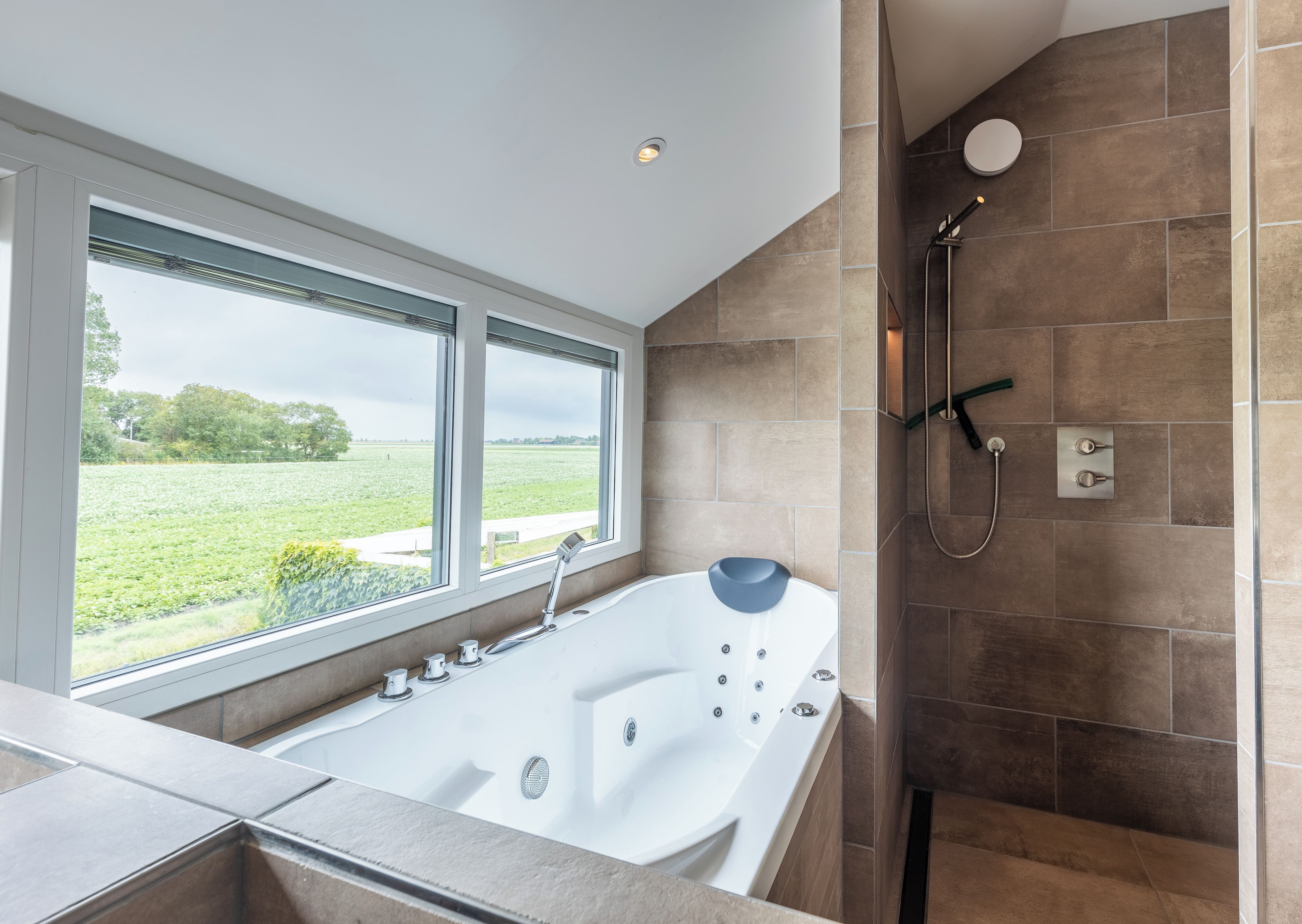 Een moderne badkamer met een groot bad, een douche en uitzicht op een groen veld door een groot raam.