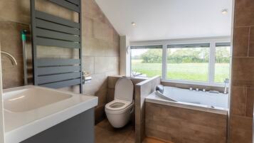 A modern bathroom with a toilet, sink, and bathtub, featuring a large window with a view of greenery.