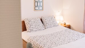 Un lit bien fait, recouvert d’une couvre-lit à motifs noirs et blancs, un tableau encadré au mur et une lampe de chevet.