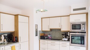 Une cuisine moderne avec des meubles blancs, un plan de travail en granit, une machine à café, un four à micro-ondes et un four traditionnel.
