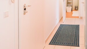 Un couloir avec une porte blanche, un téléphone, un interrupteur et un luminaire fixé au mur.