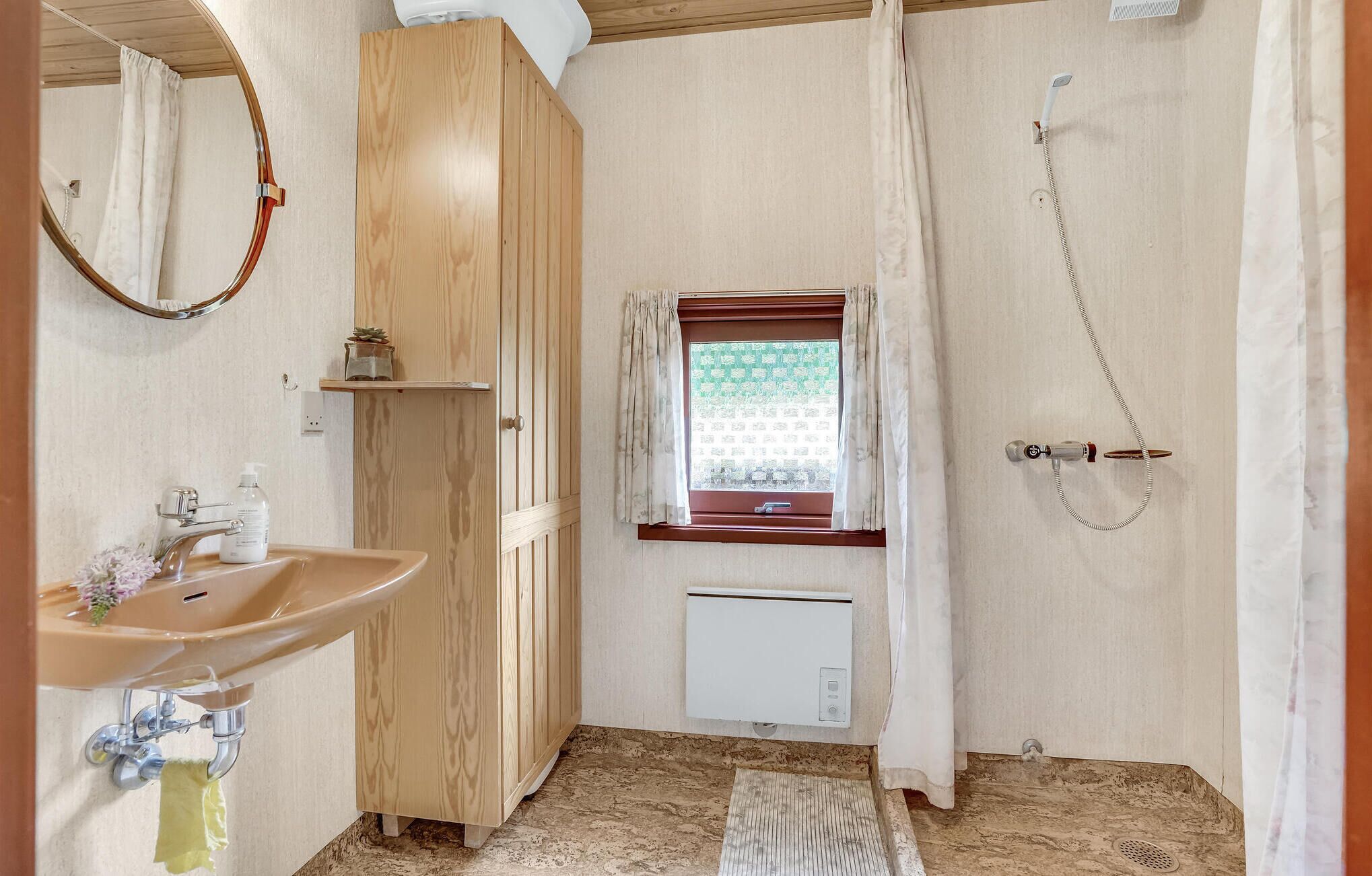 A bathroom with a wooden vanity, a sink, a mirror, a window with a view, and a shower.