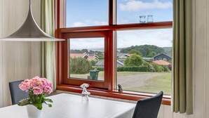 A dining area with a table, chairs, a vase of flowers, and a view of a residential neighborhood through large windows. - Stunning home in Hejls (Hejls)