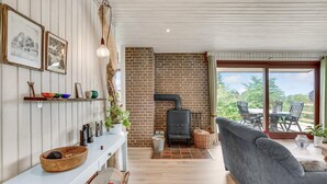 A cozy living room with a white console table, a grey sofa, a brick fireplace, and a view of greenery outside. - Stunning home in Hejls (Hejls)