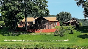 Een groot huis met terras, omringd door een verzorgd gazon en een waterpartij.
