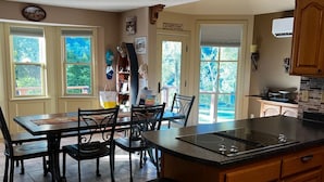 Een keuken met een centraal eiland, een eethoek met stoelen, een prullenbak en uitzicht op de omgeving door de ramen.