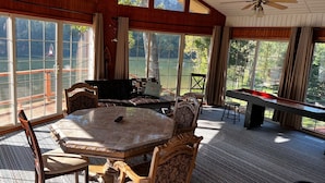 Een ruime kamer met een grote tafel en stoelen, een plafondventilator en grote ramen met uitzicht op het landschap.