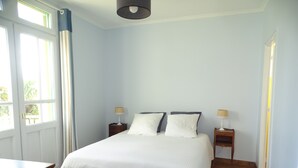 Une chambre à coucher avec un lit, deux tables de chevet, une commode en bois et une fenêtre avec des rideaux.