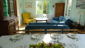 Un coin repas avec une table dressée pour quatre personnes, un canapé bleu, un fauteuil jaune et un meuble.