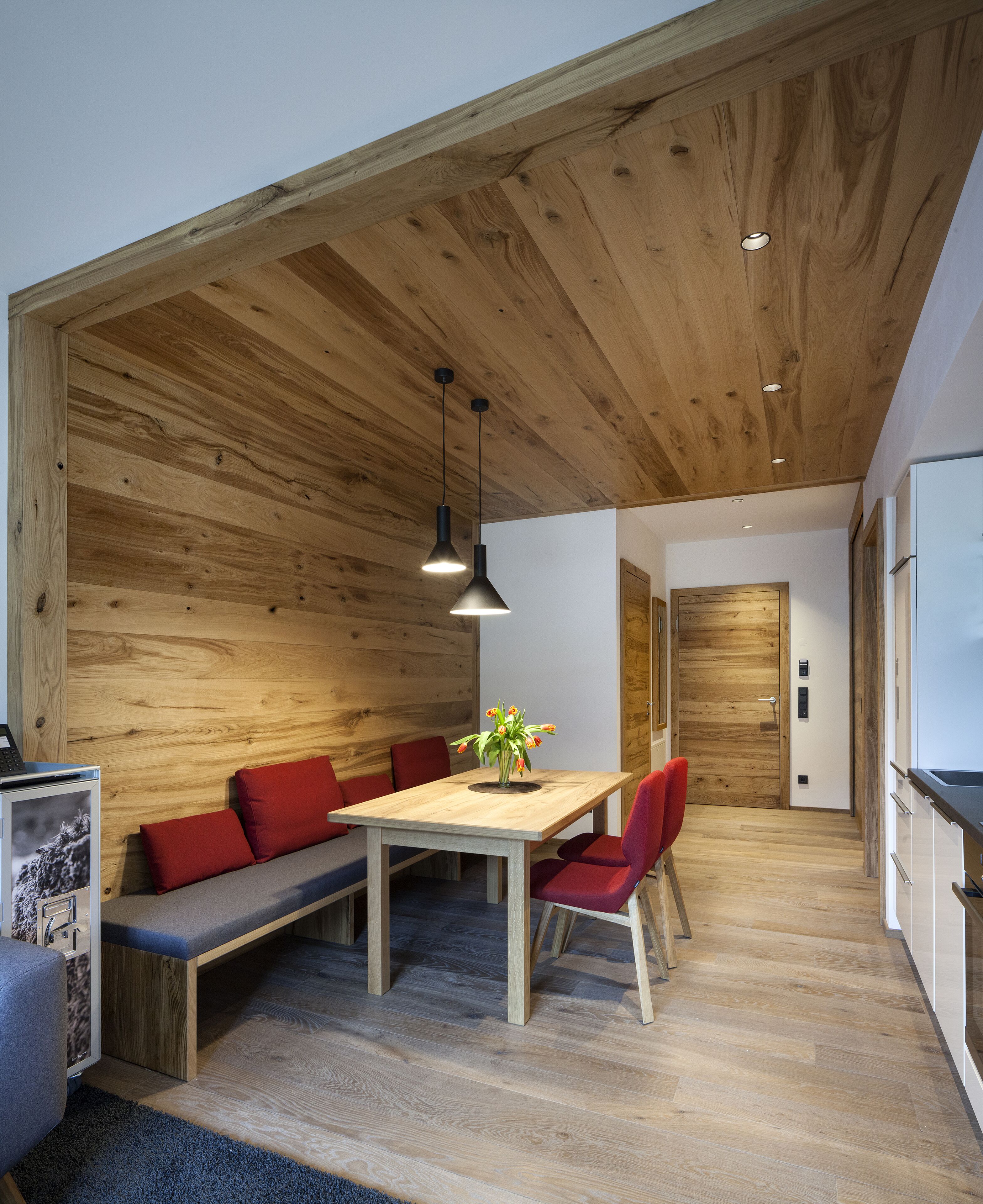 A modern kitchen with wooden cabinetry and a built-in bench with red cushions.