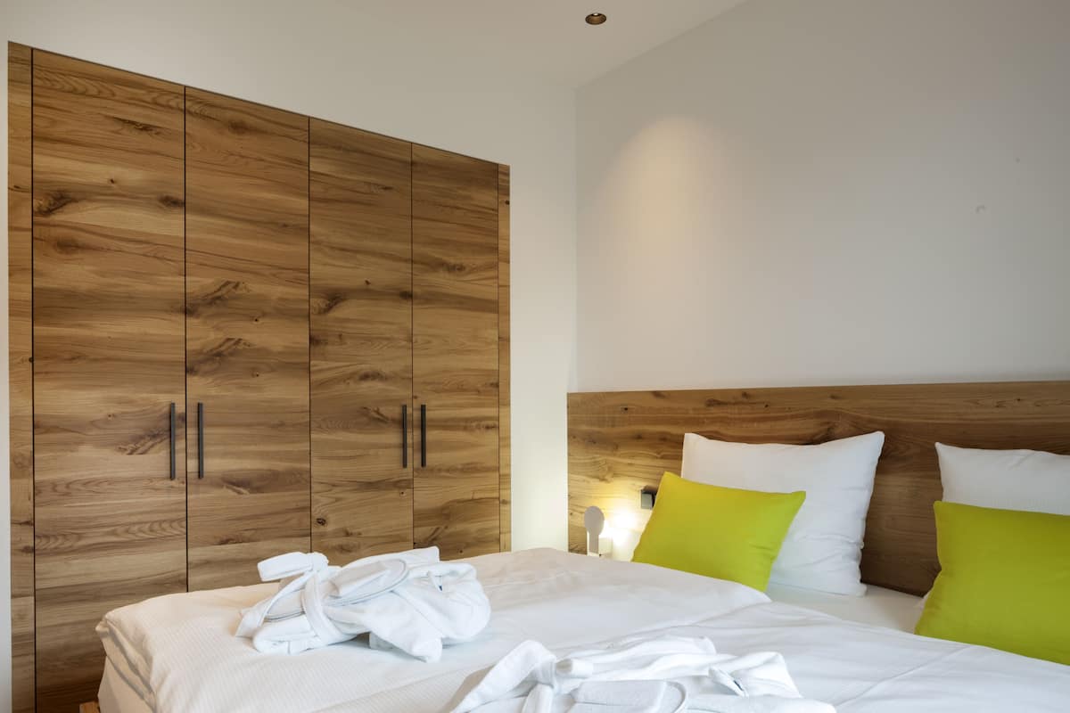 Un dormitorio con un armario de madera, una cama con ropa blanca y almohadas verdes.