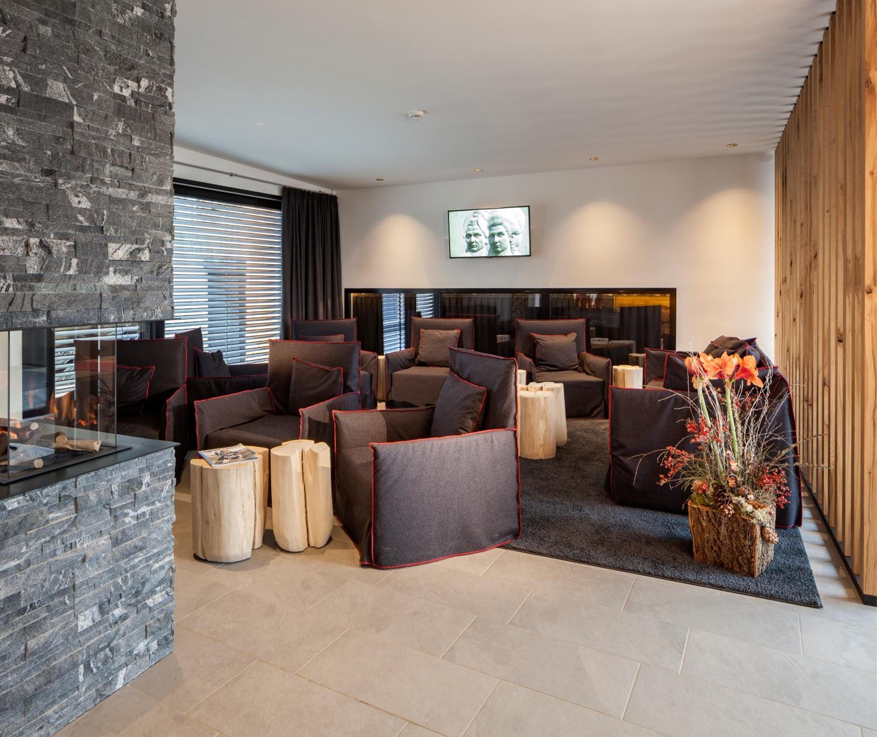Eine moderne Lounge mit Steinwand, verschiedenen Sitzgelegenheiten wie Sofas und Sesseln, einem Kamin und einem großen Fernsehbildschirm.
