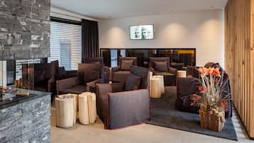 Eine moderne Lounge mit Steinwand, verschiedenen Sitzgelegenheiten wie Sofas und Sesseln, einem Kamin und einem großen Fernsehbildschirm.