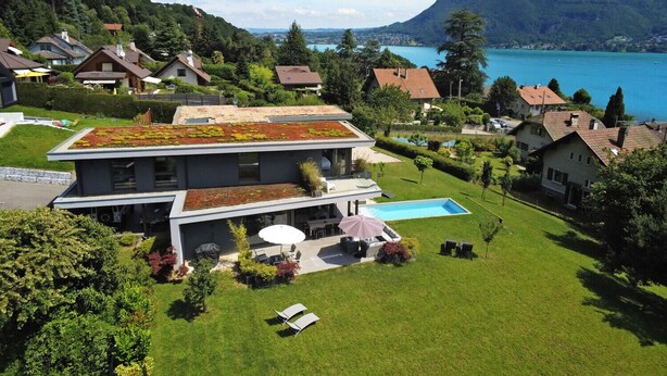 A modern house with a green roof, a swimming pool, and a view of a lake and mountains.