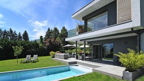 A modern two-story house with a swimming pool, outdoor seating, and a well-maintained lawn.