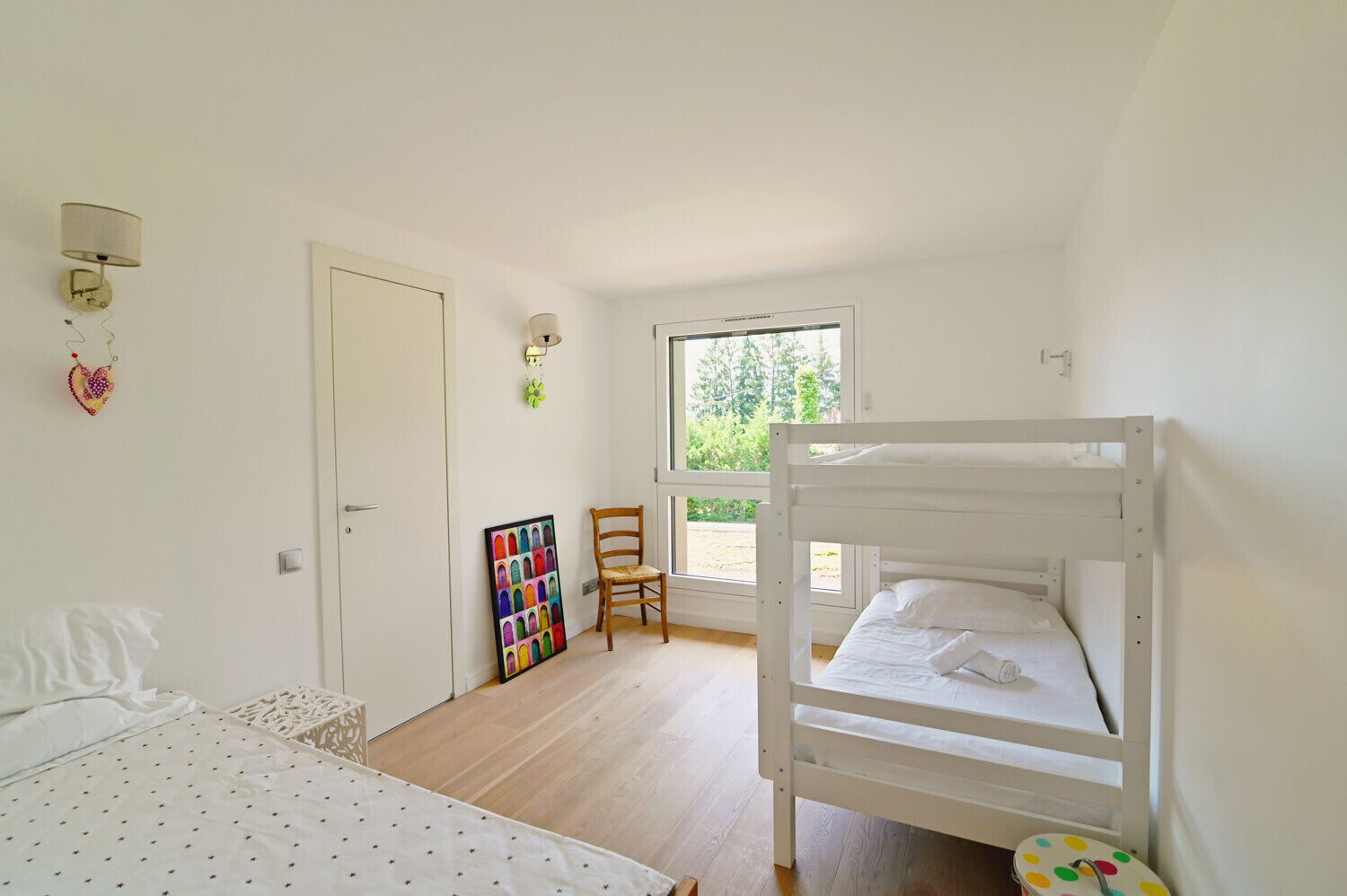 A bedroom with a bunk bed, a chair, a door, and a window.