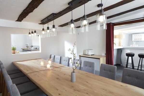 Un comedor moderno con una mesa de madera, sillas tapizadas de color gris, lámparas colgantes y un florero con flores.