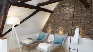 A spa room with two lounge chairs, a floor lamp, a stone wall, and a wooden ladder.