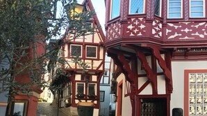 A narrow cobblestone street lined with traditional half-timbered houses, each with distinct window patterns and a sign indicating a restaurant.