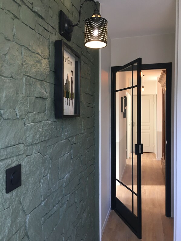 A hallway with a stone wall, a framed picture, a black door, and a hanging light fixture.