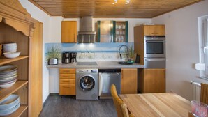 Une cuisine compacte avec des meubles en bois, un lave-linge encastré et un coin repas comprenant une table et des chaises.