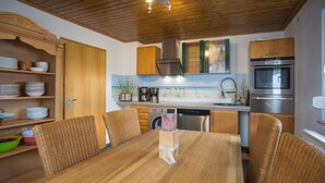 Une cuisine compacte avec des meubles en bois, un four encastré et un coin repas comprenant une table en bois et des chaises en osier.