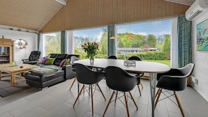 A modern living room with a dining area, large windows, and a view of a house and greenery. - Beautiful home in Aabenraa with WiFi (Aabenraa)