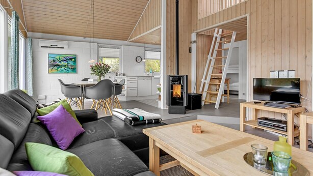 A modern interior with a black leather sofa, wooden coffee table, and a kitchen area with a stove. - Beautiful home in Aabenraa with WiFi (Aabenraa)