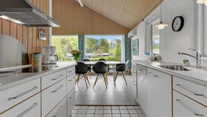 A modern kitchen with white cabinetry, a stainless steel range hood, a dining area with black chairs, and a view of the outdoors. - Beautiful home in Aabenraa with WiFi (Aabenraa)