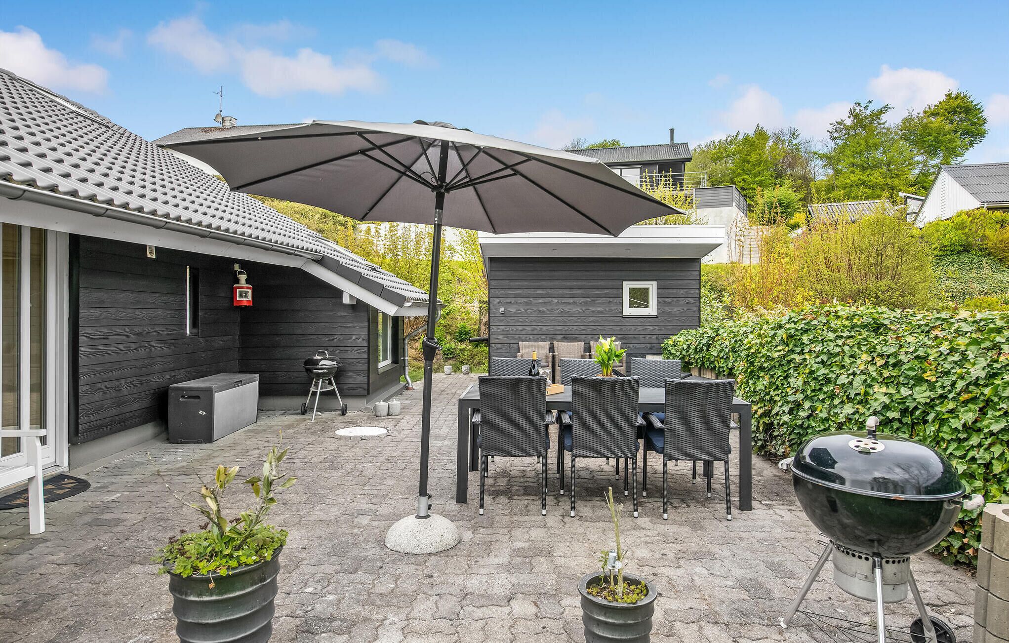 A patio area with a table and chairs, a barbecue grill, and potted plants.