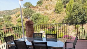 A covered outdoor patio with a table and chairs, a brick pillar, and a view of a hilly landscape. - Villa El Olivo, rural villa with pool (Alcaucín)