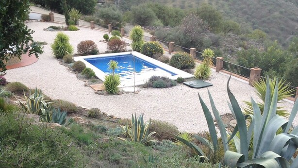 A pool surrounded by gravel and various plants, with a hillside in the background. - Villa El Olivo, rural villa with pool (Alcaucín)