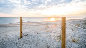 Une barrière faite de cordes sur une plage de sable, avec un coucher de soleil en arrière-plan.