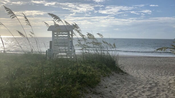 Una playa con una torre de salvavidas, arena y vista al océano.