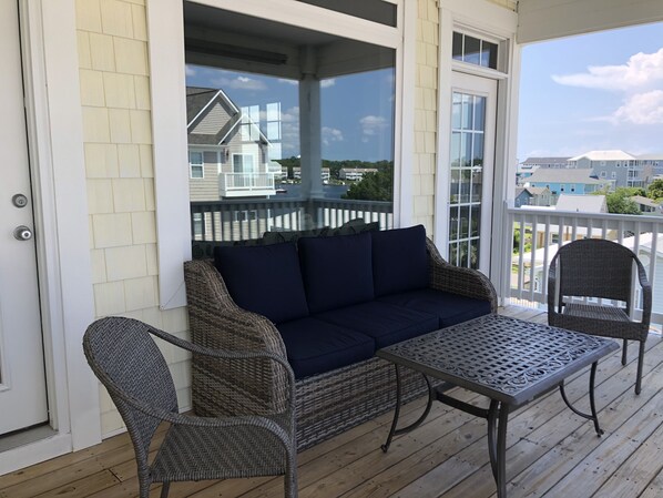 A covered porch with wicker furniture, a dark blue sofa, and a metal table.