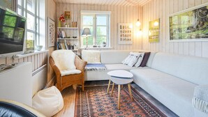 Een gezellige woonkamer met een witte bank, een rieten fauteuil, een klein rond tafeltje en een kamerkleed met dessin.
