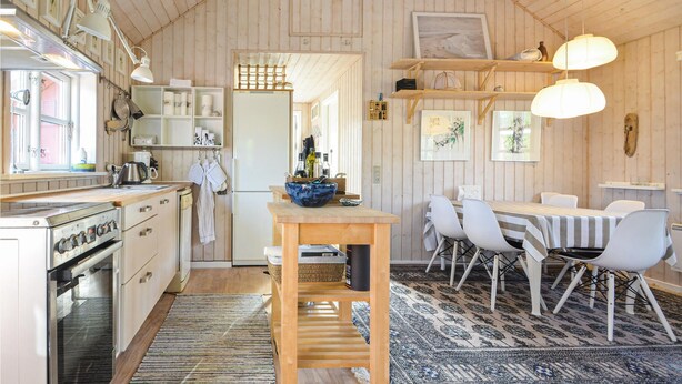 Een gezellige keuken met houten wanden, een eethoek met witte stoelen en een centraal kookeiland met een kom.